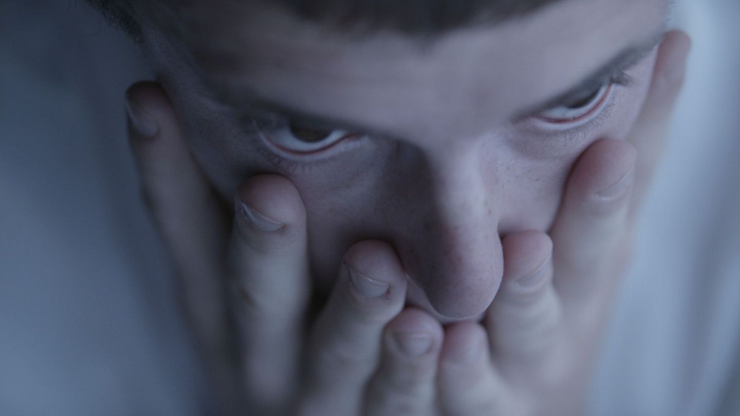 Close up of a face from a bird's eye view, the person covers their mouth with their hands